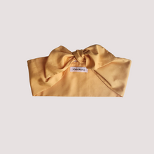 Load image into Gallery viewer, A golden yellow cotton hair scarf tied in a knot on a textured background.