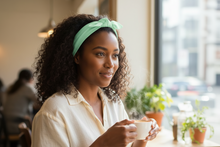 Load image into Gallery viewer, Mint green cotton hair scarf worn by a woman with curly hair, sitting in a cafe holding a cup.