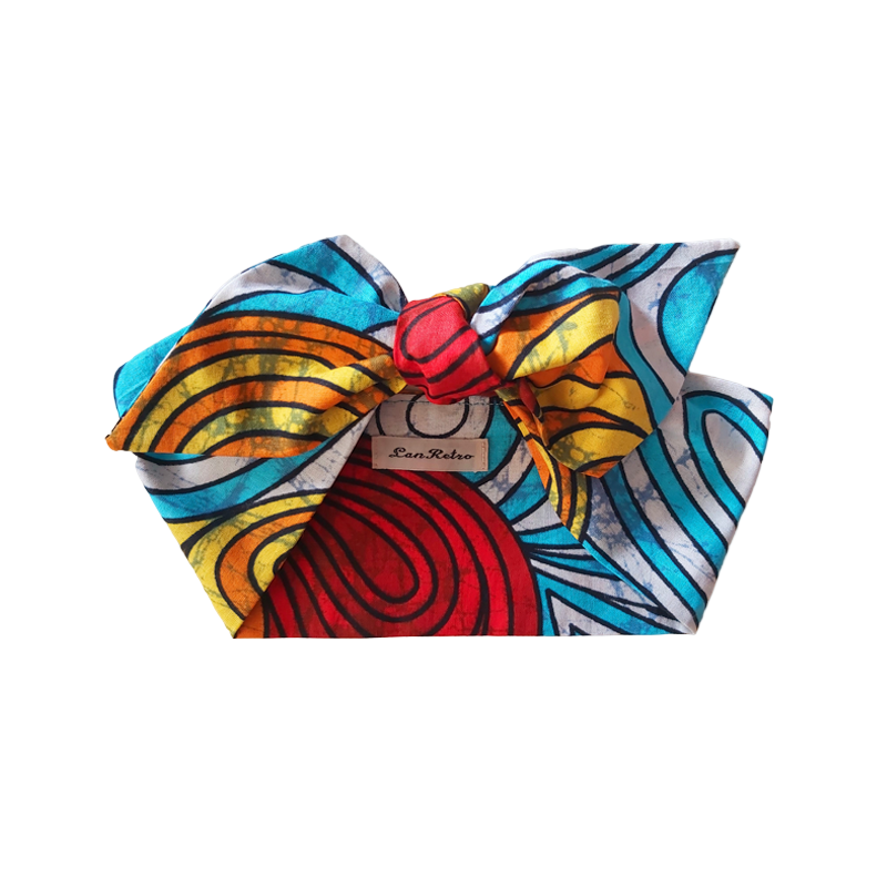 A colourful Ankara cotton hair scarf displayed on a neutral background, featuring blue, yellow, and other vibrant hues in a patterned design.