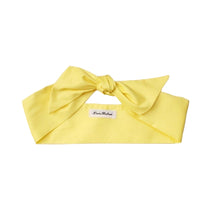 Load image into Gallery viewer, A yellow cotton hair scarf laid out on a white background, showing a bow knot at one end with a tag visible.