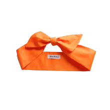 Load image into Gallery viewer, An orange cotton hair scarf displayed on a white background with a label showing the brand name.