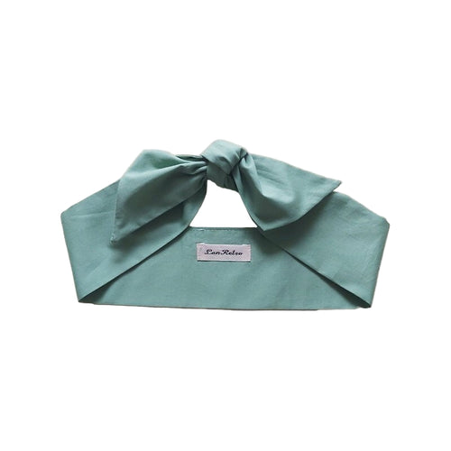 A sage green cotton hair scarf tied in a bow, displayed on a flat surface.