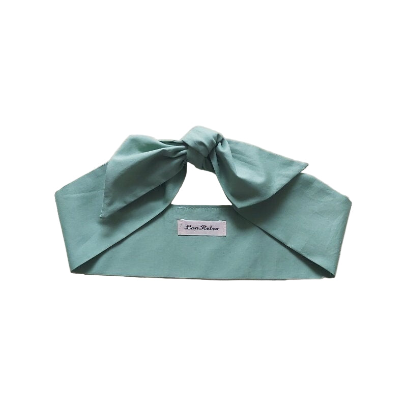A sage green cotton hair scarf tied in a bow, displayed on a flat surface.